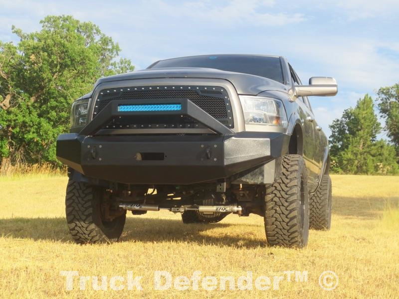 A black pickup truck with a custom TDS aluminum bumper on a grass field clearing with trees around.